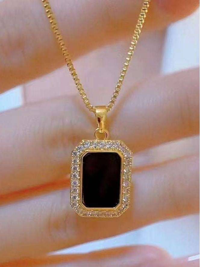 Close-up of black rectangular pendant with white CZ surround held between fingers