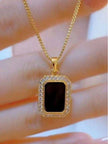 Close-up of black rectangular pendant with white CZ surround held between fingers