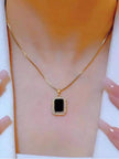 Gold-plated black pendant necklace worn on a woman's collarbone against a white top