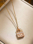 Rose gold bag charm pendant necklace with cubic zirconia pavé and H clasp displayed on a cream cushion
