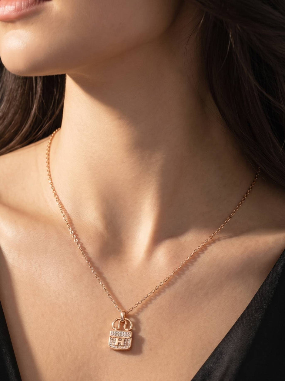 Model wearing rose gold Constance bag charm pendant necklace against a black top, close-up neck shot