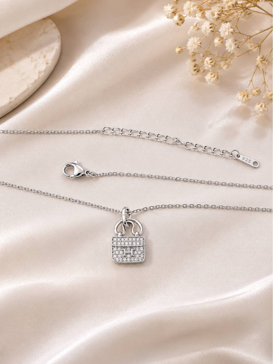 Full view of silver bag charm necklace laid flat on ivory satin fabric showing lobster clasp and 925 stamp