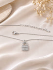 Full view of silver bag charm necklace laid flat on ivory satin fabric showing lobster clasp and 925 stamp