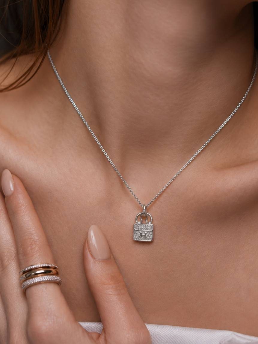 Woman wearing silver zirconia bag pendant necklace at collarbone with stacked rings on hand
