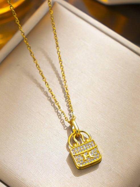 Gold-plated handbag pendant necklace with cubic zirconia stones displayed on a cream jewellery tray