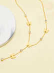 Gold butterfly lariat necklace laid on a cream surface beside a marble disc, highlighting the drop chain with butterfly and crystal detailing