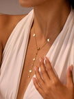 Model wearing gold butterfly lariat necklace over a white halter dress, showing how the drop falls elegantly at the neckline