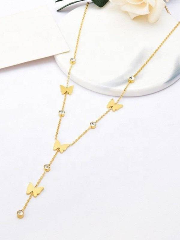 Gold butterfly lariat necklace flat lay on white surface near flowers, showing full chain length and cascading butterfly and rhinestone drop