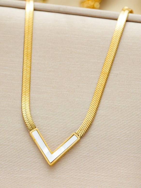 Gold-plated herringbone necklace with white shell V-shape pendant laid flat on cream fabric