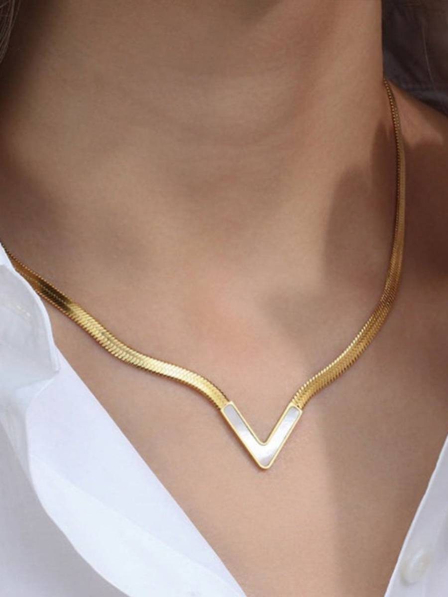 Gold herringbone V-shape necklace worn at the collarbone with a white open-collar shirt