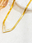 Close-up of gold V-shape shell pendant necklace resting on a white textured surface