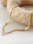 Gold herringbone necklace with chevron shell pendant draped over a smooth beige stone prop
