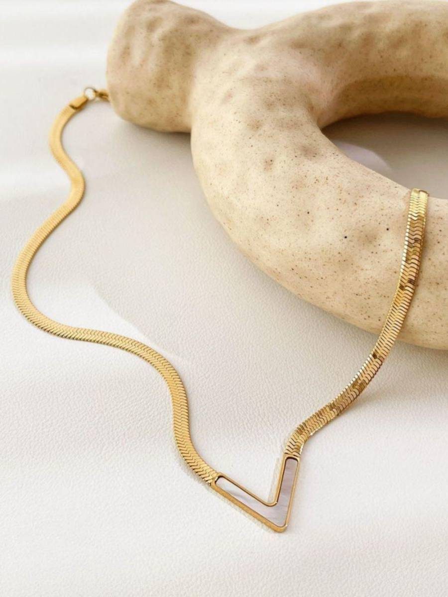 Full length gold herringbone V-necklace with shell pendant displayed on white surface with stone prop
