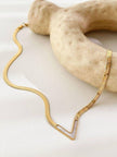 Full length gold herringbone V-necklace with shell pendant displayed on white surface with stone prop