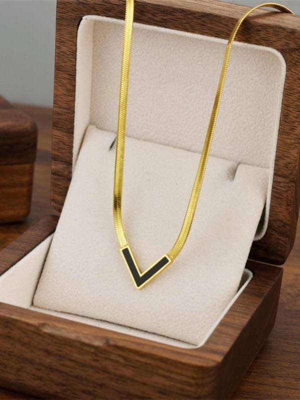 Gold herringbone V-shape necklace with black enamel pendant displayed in a wooden jewellery box