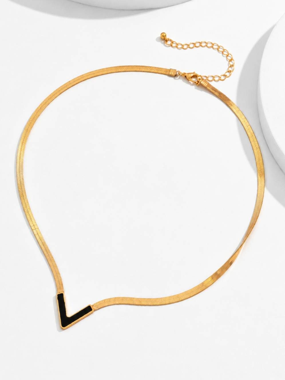 Gold-plated black enamel V necklace laid flat on a white surface showing full chain and lobster clasp
