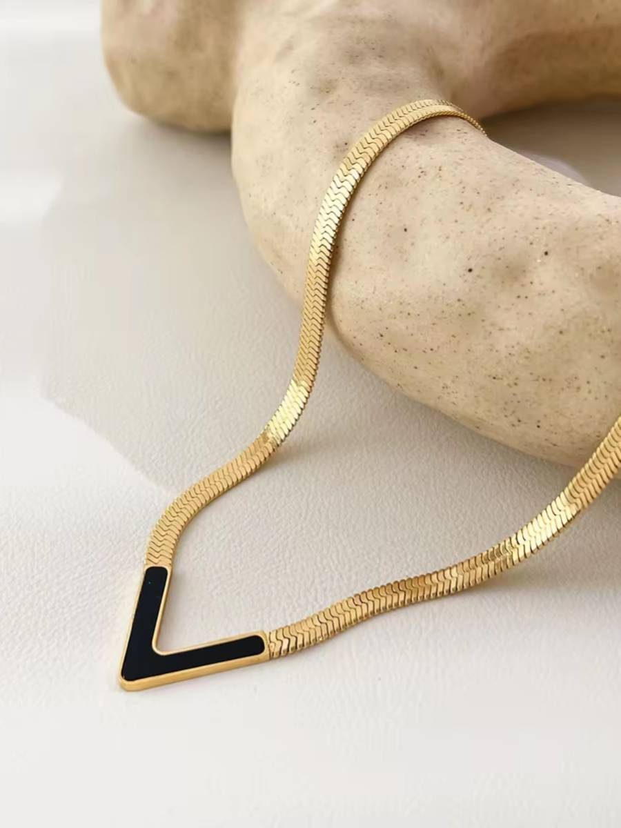 Close-up of gold herringbone chain and black enamel V pendant draped over a stone prop