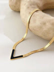Close-up of gold herringbone chain and black enamel V pendant draped over a stone prop