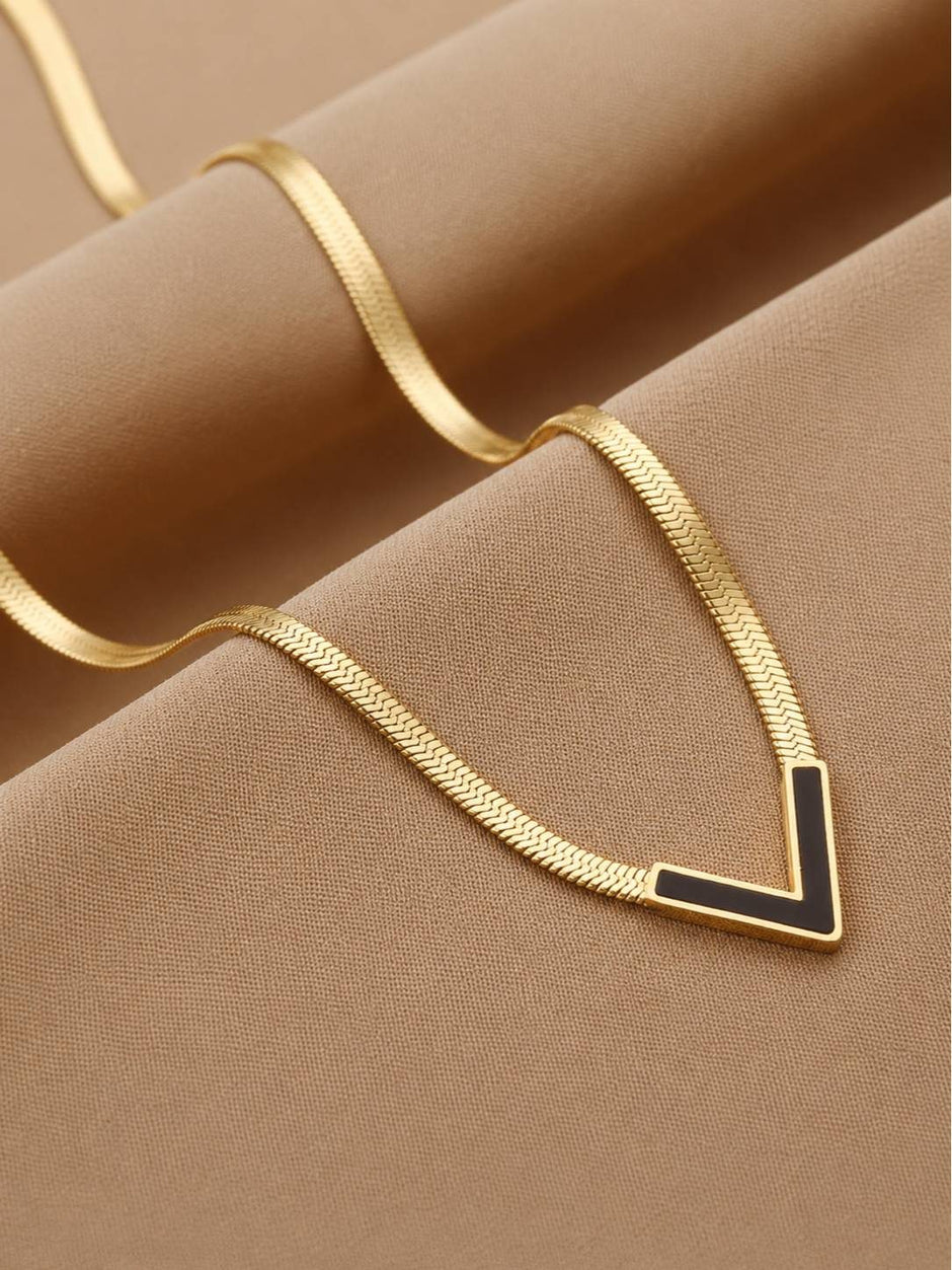 Gold flat herringbone necklace with black V pendant arranged in a wave on camel fabric