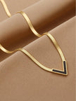Gold flat herringbone necklace with black V pendant arranged in a wave on camel fabric