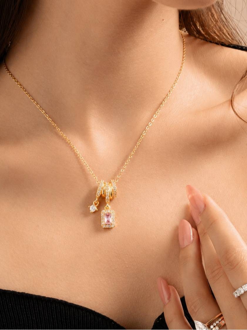 Woman wearing gold-plated CZ charm necklace at collarbone with black top and manicured hand