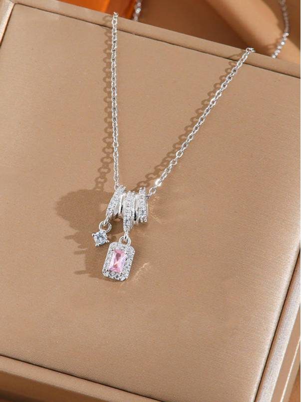 Silver pendant necklace with pink emerald-cut zirconia and round solitaire charm on beige jewellery tray