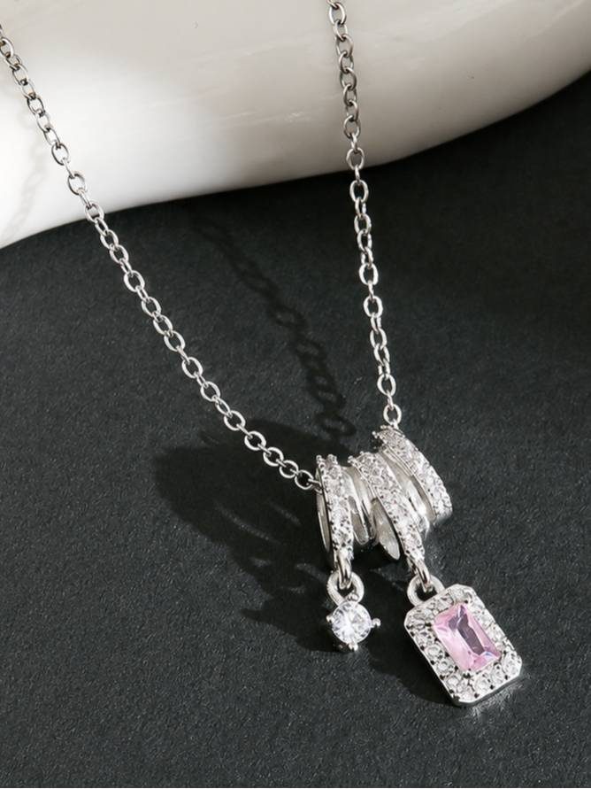 Close-up of silver layered ring bail with pavé zirconia and pink stone drop pendant on dark surface