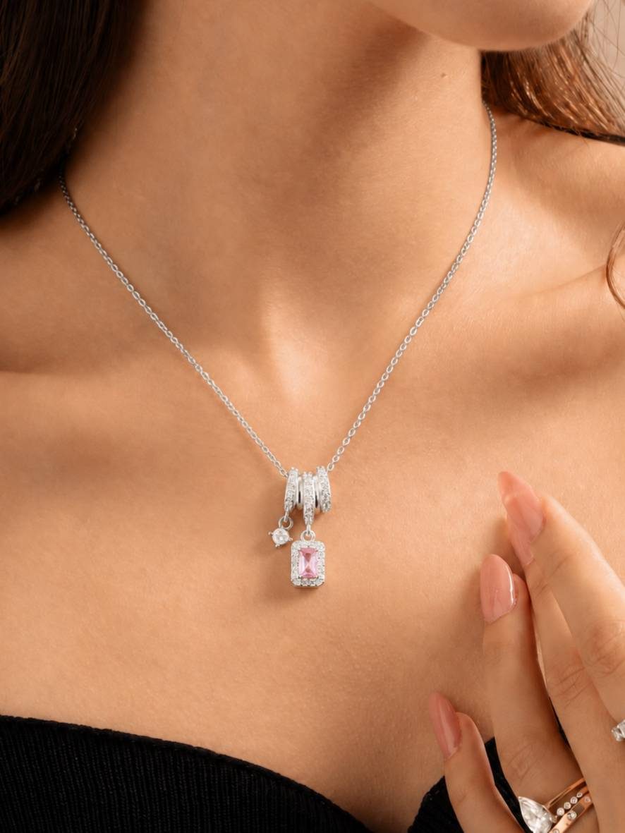Woman wearing silver zirconia pendant necklace over black top, hand resting on chest