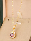 Gold-plated teardrop pendant necklace with purple CZ stone displayed in a cream jewellery box