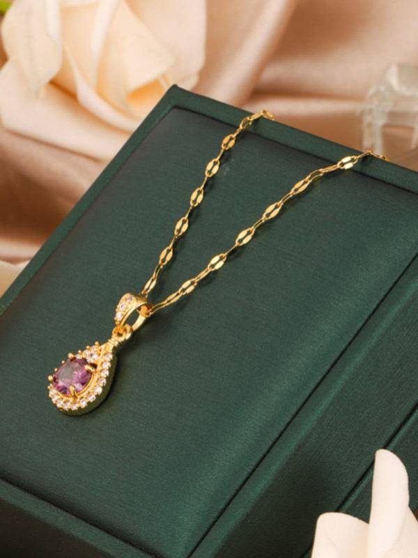 Purple CZ teardrop pendant necklace laid flat on a green velvet jewellery box with a peach flower beside it