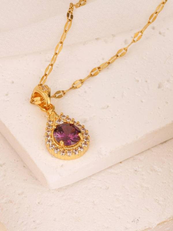 Gold-plated purple CZ pendant necklace resting on a white stone surface showing the oval-link chain