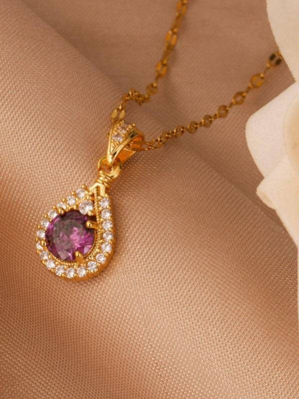 Teardrop gold pendant with purple cubic zirconia centre and white CZ halo lying on a beige fabric surface