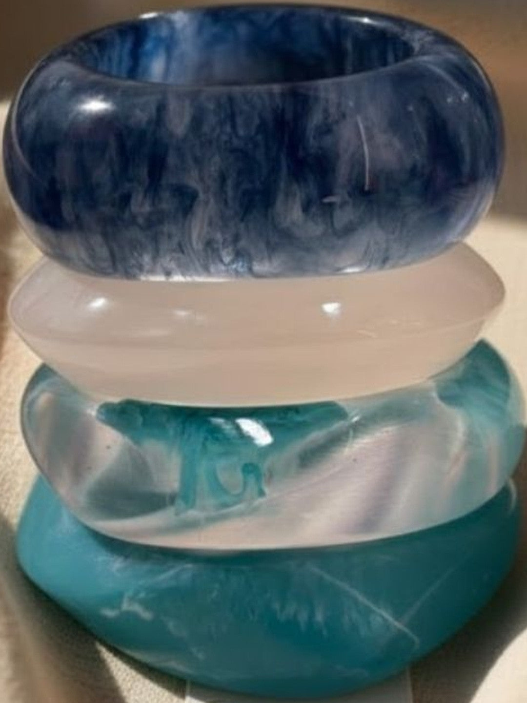 Close-up of four chunky marbled resin bangles stacked together showing swirl detail in blue and teal tones