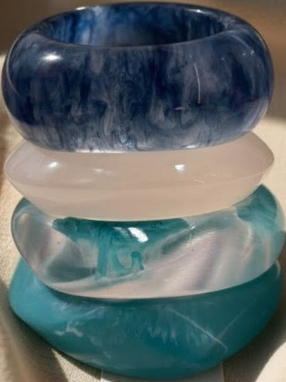 Close-up of four chunky marbled resin bangles stacked together showing swirl detail in blue and teal tones