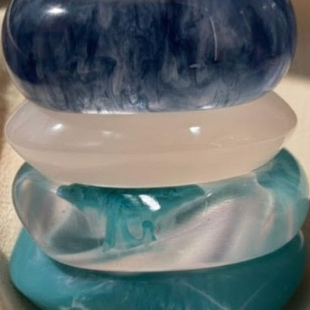 Close-up of four chunky marbled resin bangles stacked together showing swirl detail in blue and teal tones