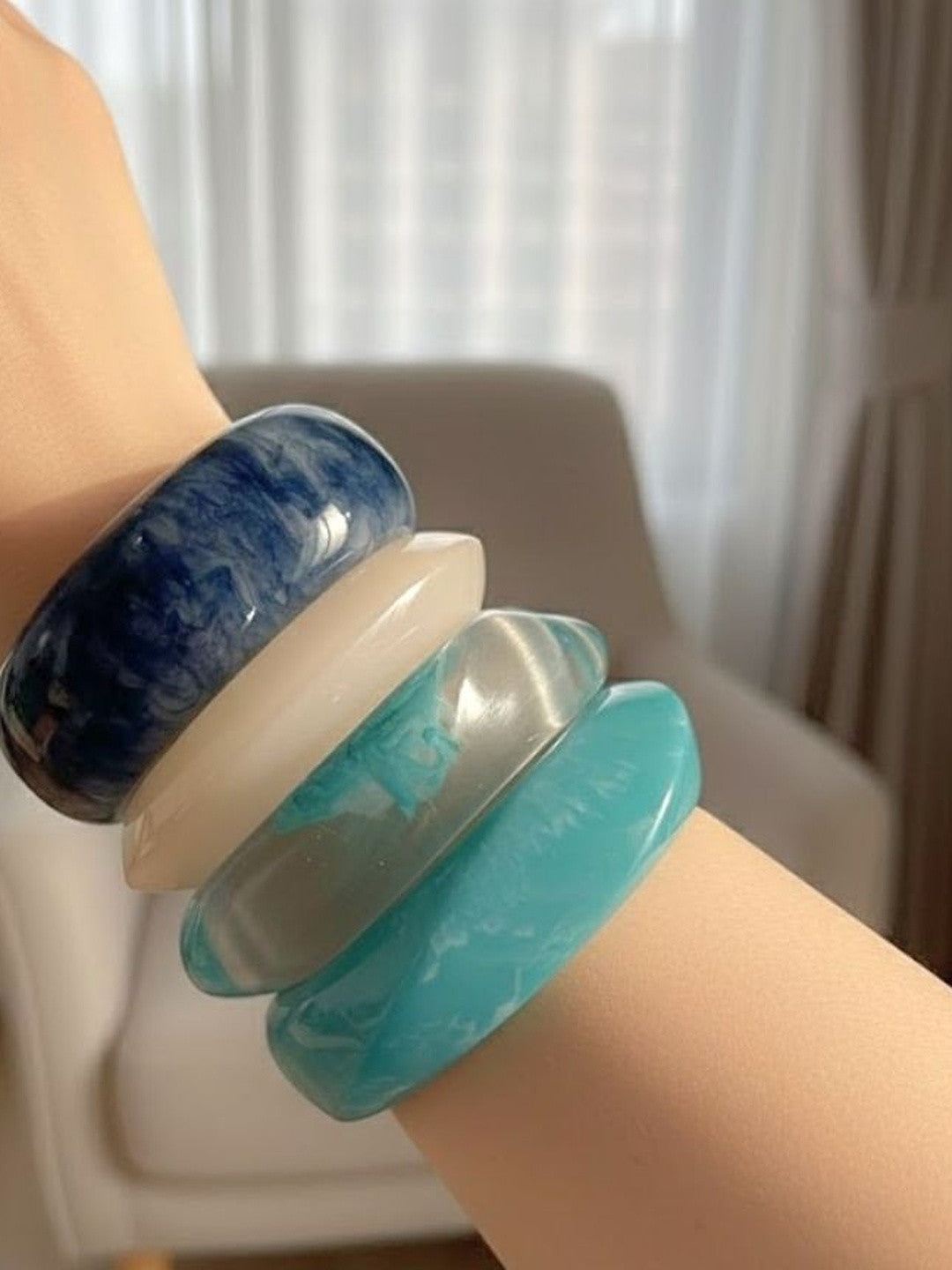 All four marbled resin bangles worn stacked on a wrist showing scale and fit in natural light