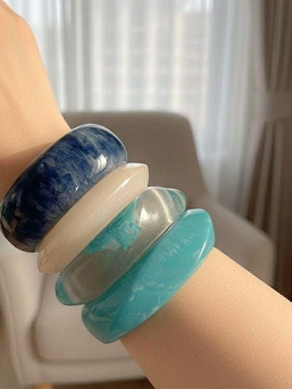 All four marbled resin bangles worn stacked on a wrist showing scale and fit in natural light