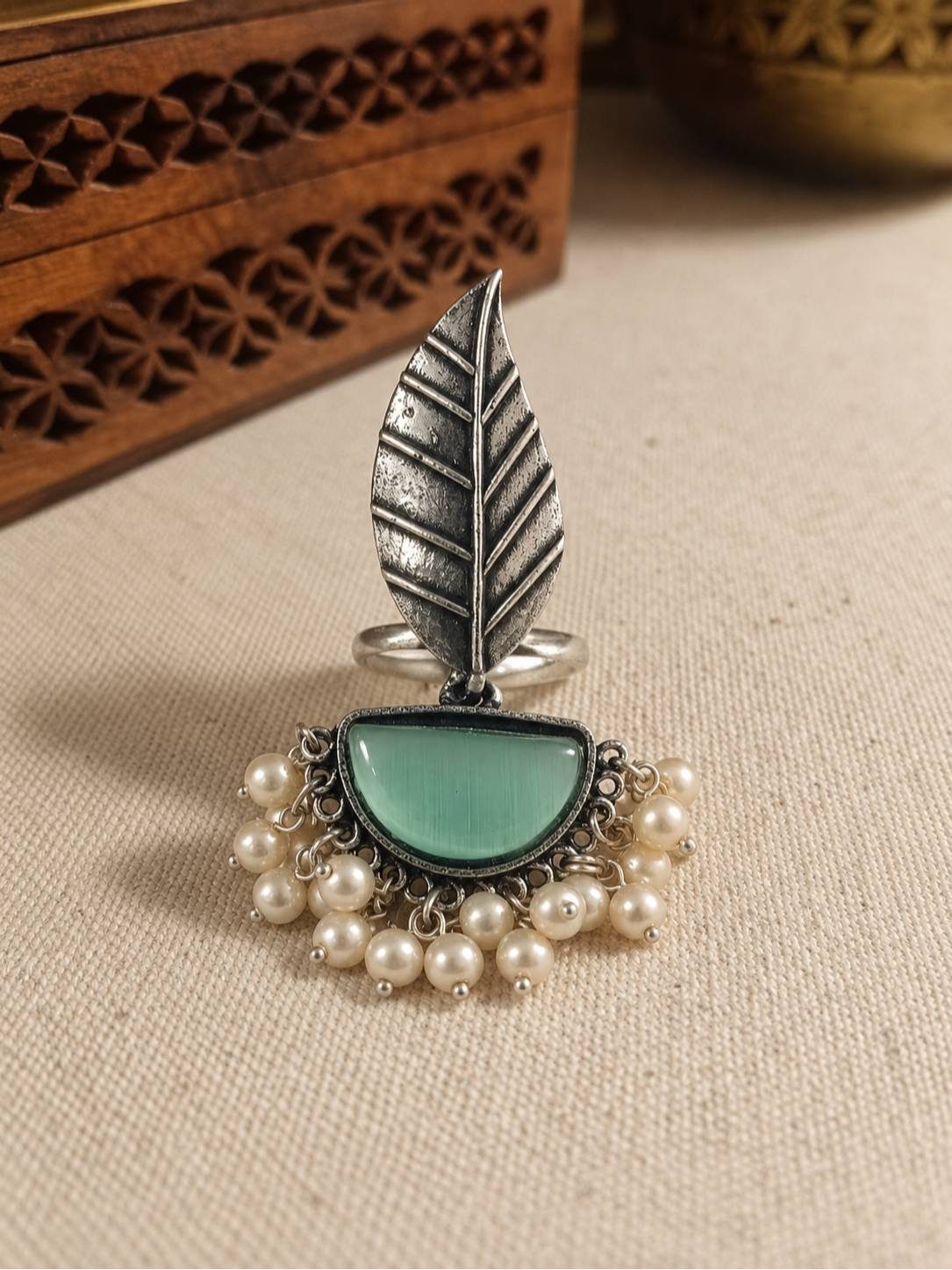 Front view of oxidised silver leaf ring with mint cat eye stone and ivory pearl drops on linen surface