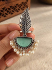 Close-up of oxidised silver leaf ring held in hand showing feather texture and dangling pearl drops