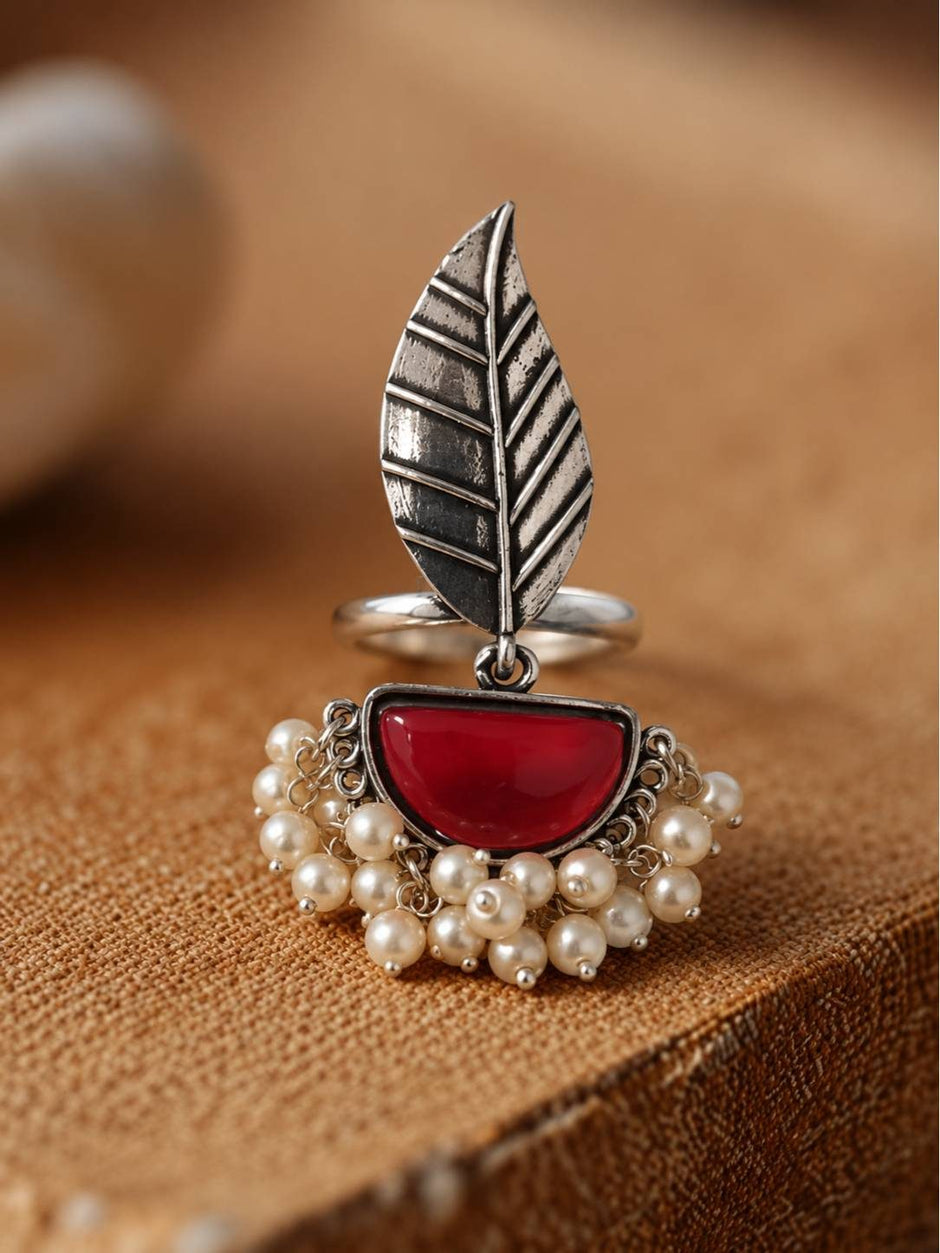 Oxidised silver leaf ring with red half-moon stone and pearl drops displayed upright on burlap surface