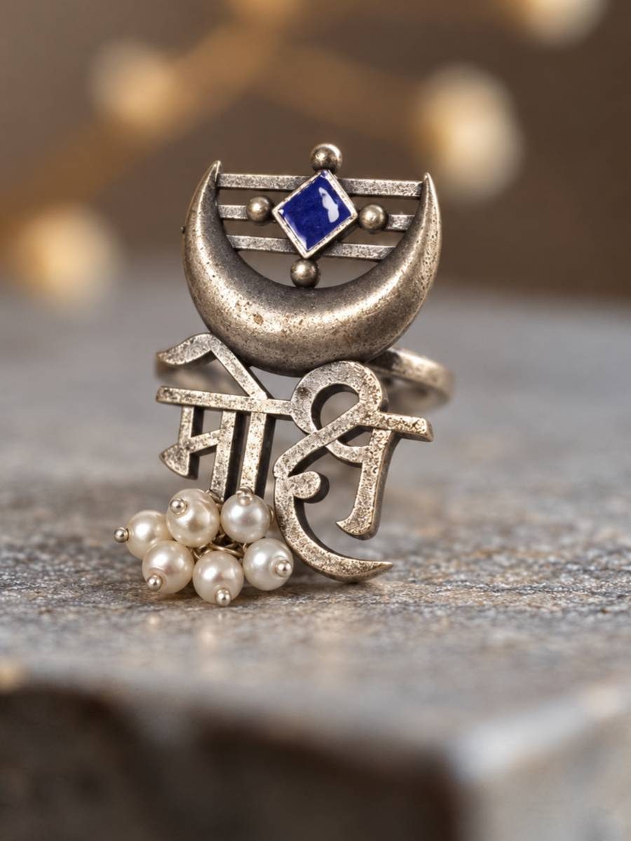 Oxidised silver Mohi Devanagari script ring with crescent moon, blue enamel stone and ivory pearl drops, resting on stone surface