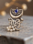 Oxidised silver Mohi Devanagari script ring with crescent moon, blue enamel stone and ivory pearl drops, resting on stone surface