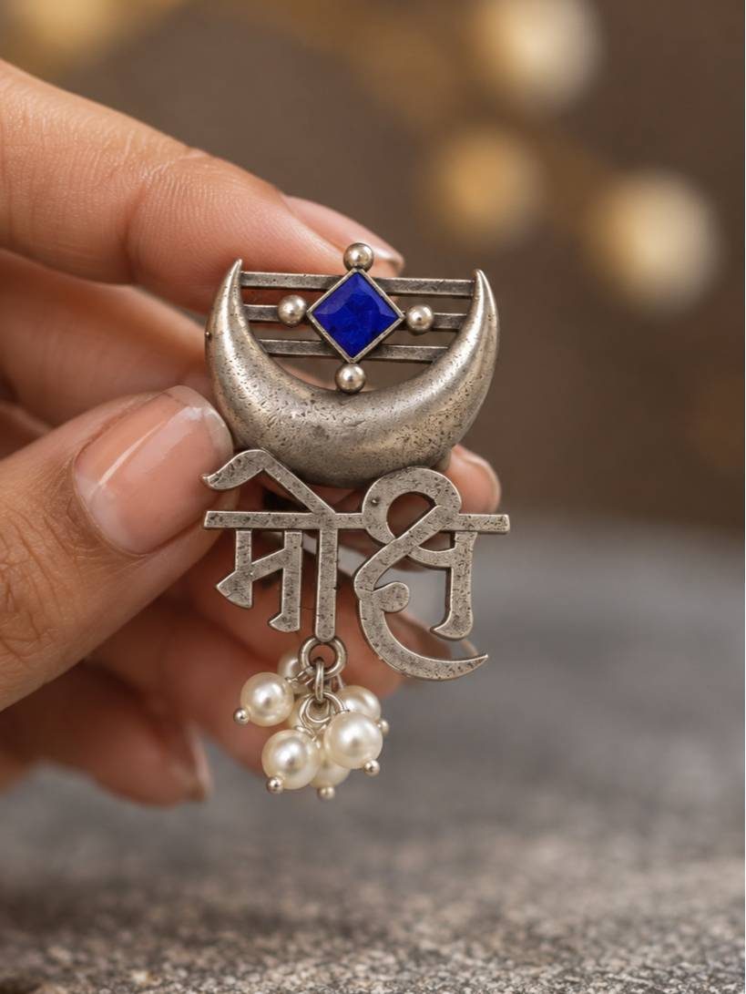 Close-up of Mohi script ring held between fingers showing blue enamel diamond stone and dangling pearl cluster