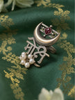 Oxidised silver Moksh script ring with crescent moon, red stone and pearl drops laid flat on green brocade fabric