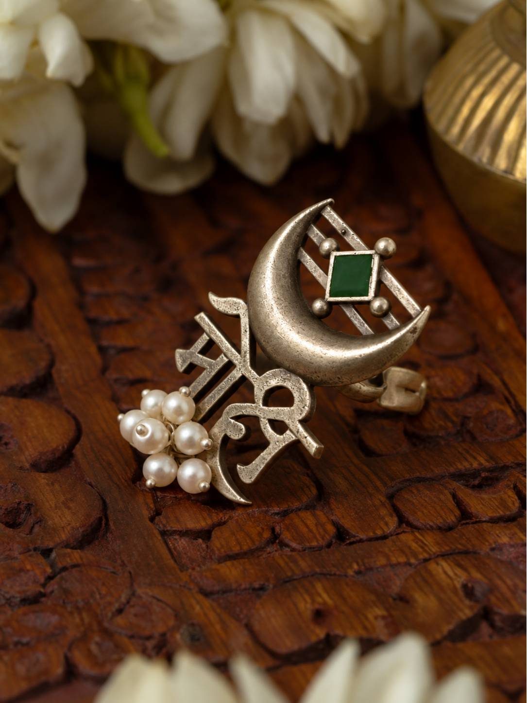 Oxidised silver Mohi script ring with crescent moon motif and pearl drops resting on carved wooden surface beside white flowers