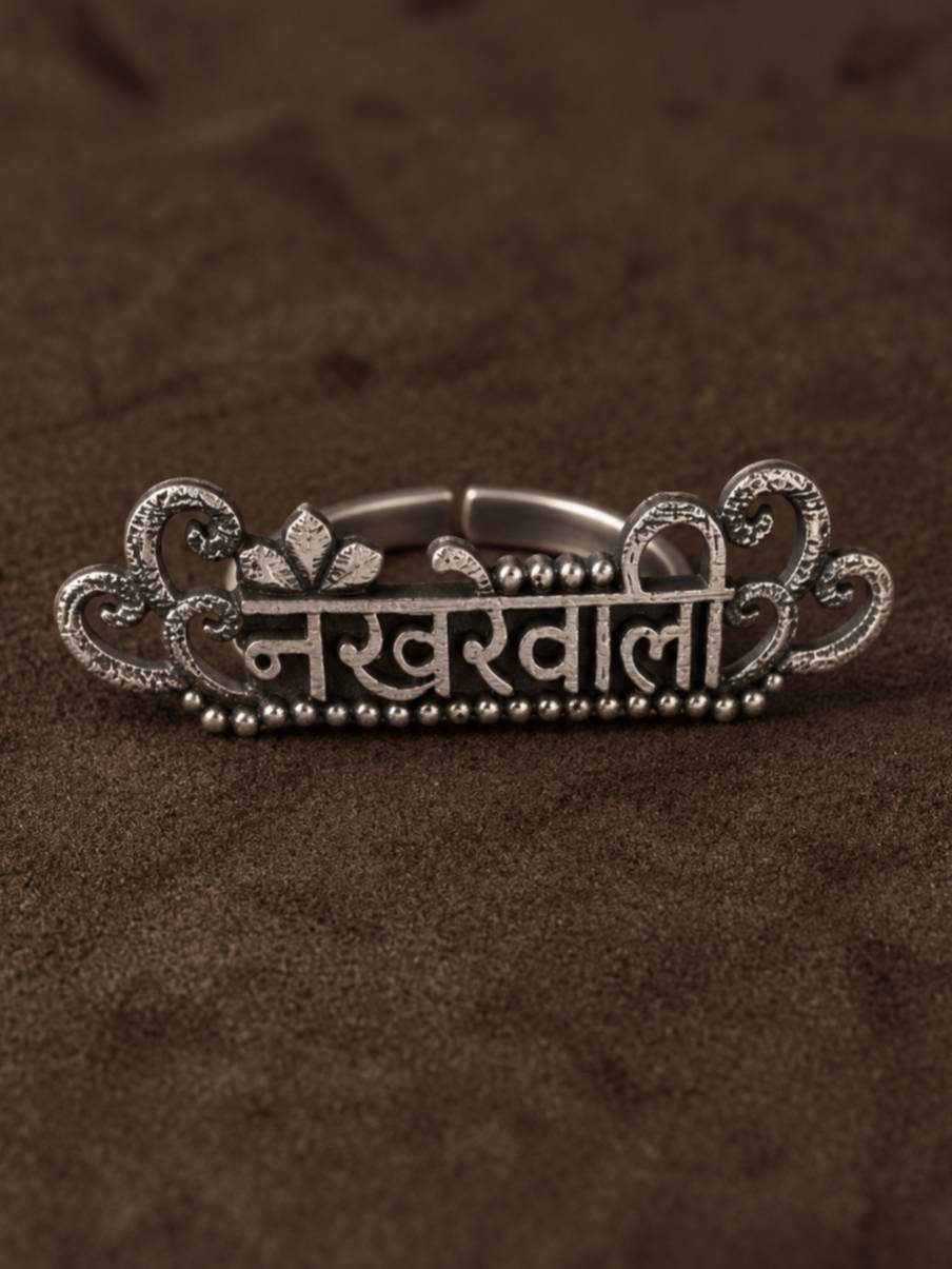 Oxidised silver Nakhrewaali ring laid flat on dark brown surface showing Devanagari inscription and filigree scrollwork