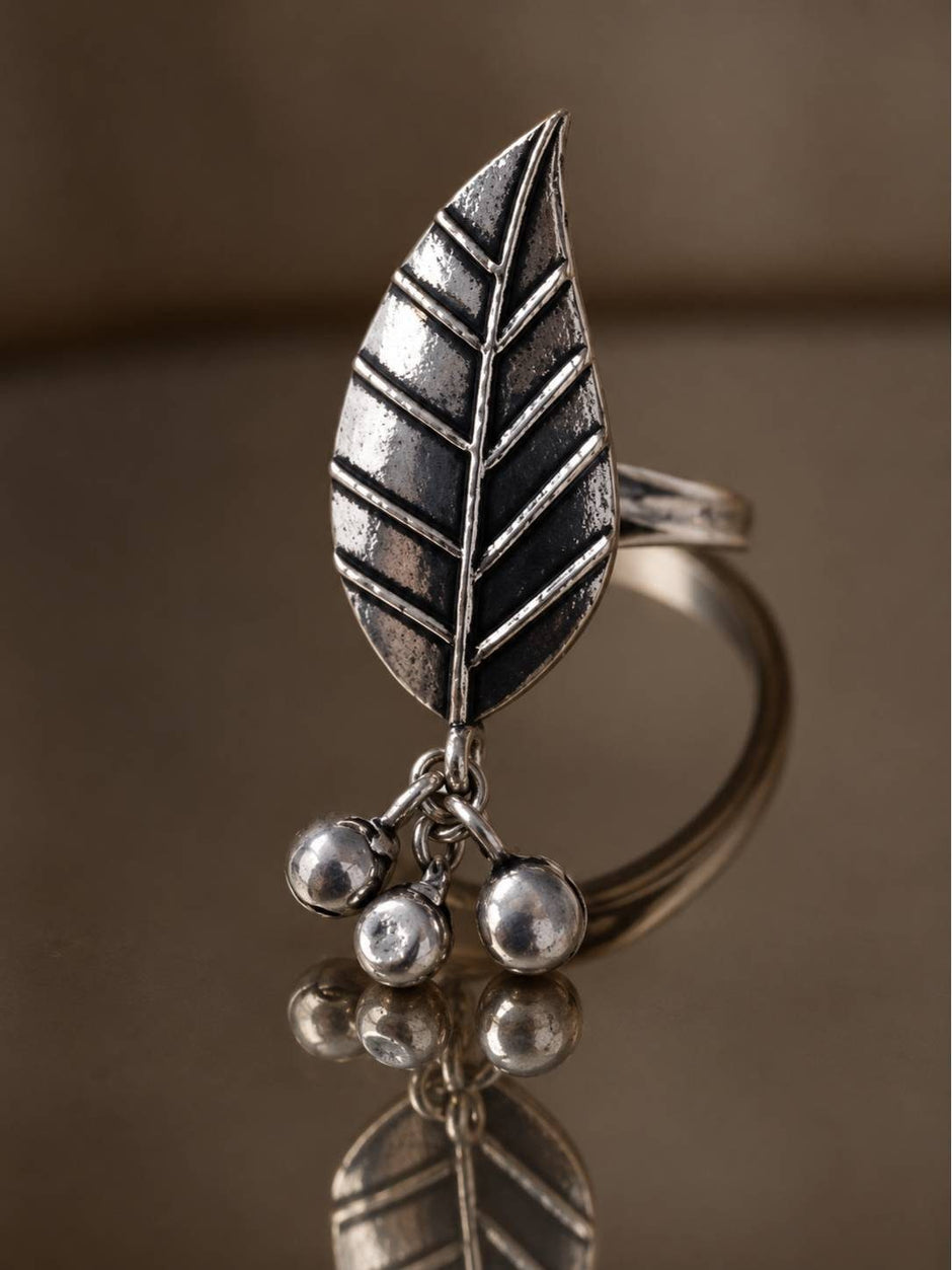 Oxidised silver leaf ring with three ghungroo ball charms resting on a reflective surface
