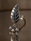 Oxidised silver leaf ring with three ghungroo ball charms resting on a reflective surface
