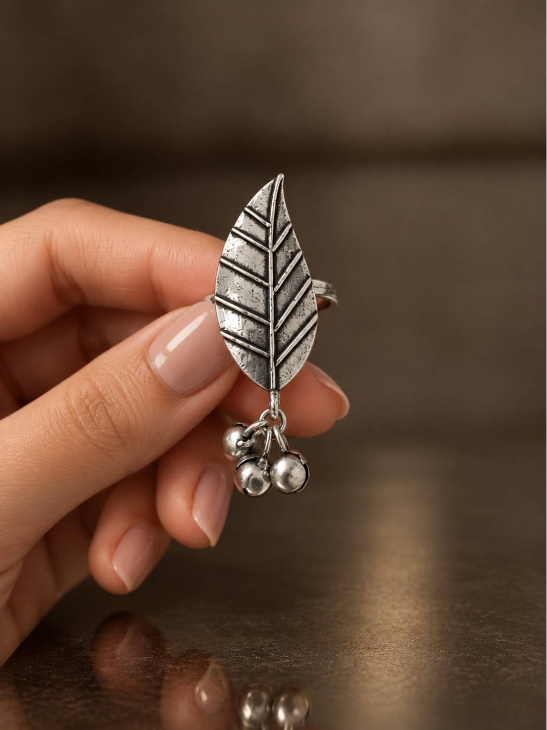 Hand holding oxidised silver leaf ring close up showing veined leaf detail and dangling ghungroos