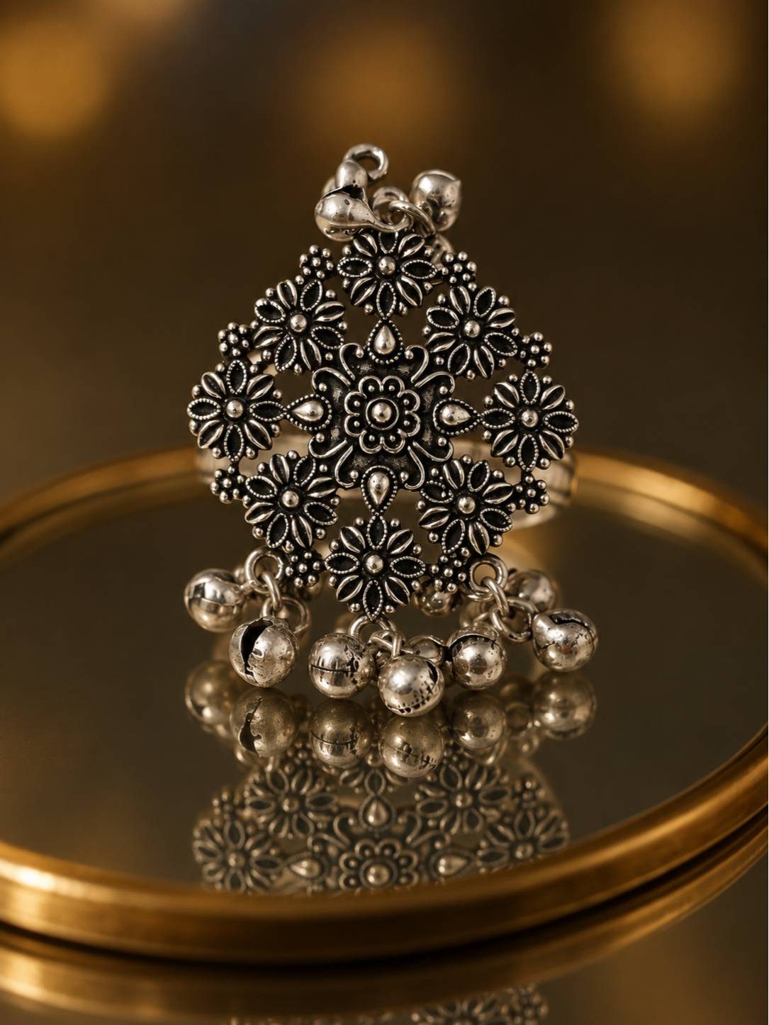 Front view of oxidised silver floral ring with ghungroo bells on a gold mirror tray